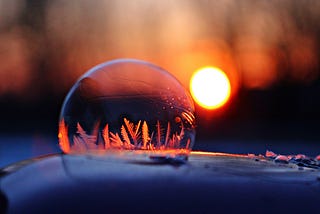 A close-up image of a frozen crystal bubble, with delicate ice formations that resemble tiny ferns. The bubble glows in the soft light of the setting sun, creating an enchanting winter atmosphere.
