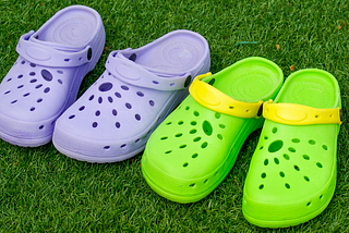 Pair of purple and green crocs on some grass
