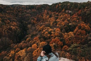 woman at the top of a mountain peak gazing out over foliage