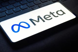 Meta logo with blue infinity symbol and “Meta” text on smartphone screen over dark laptop keyboard.