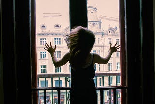 Woman pushing against a window, looking across at an old street.