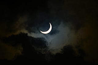 Crescent moon behind a thin cloud.