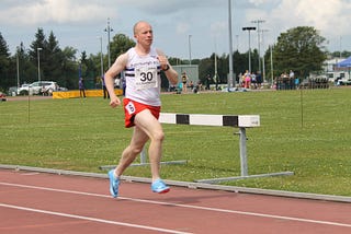 Male athlete running on a track, concentrating really hard, and conspicuously on his own.