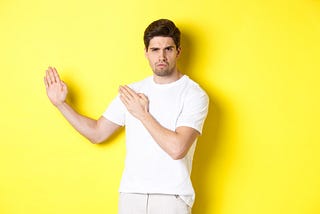 Man showing kung-fu skills, standing in white t-shirt on a yellow background.