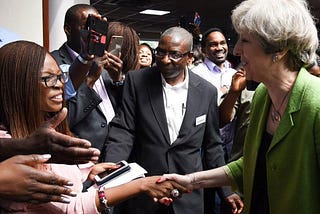 Former Prime Minister Theresa May shaking hands with Jesus House representatives, with press surrounding them.