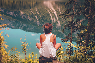 Woman sitting alone on a cliff overlooking a river.