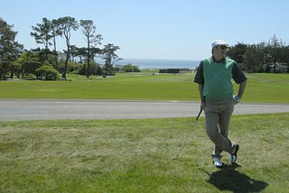 Eric leaning on a club at Pebble Beach, ocean in the background
