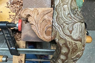 Antique carved chair leg with replacement side carving, in clamps after finishing carving.