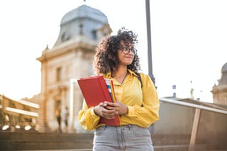 A woman in a yellow jacket holding a red book.