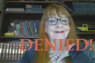 Red haired woman in front of book shelf …denied written across her in red.