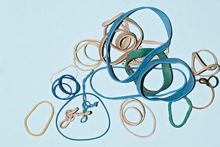 Lots of different circular rubber bands on a bright background thrown on top of each other. Some are twisted, others are nearly round.