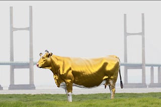 Image of a cow made of gold standing in a field in front of a bridge, representing the golden calf