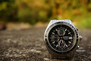 A silver watch placed on the ground outdoors