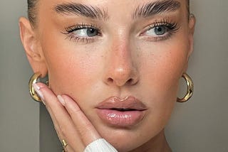 A clean looking woman with clear skin, glossy lips, slicked back hair, and gold hoop earrings.