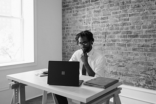 A man working at a computer in front of a brick wall.