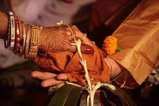 Scene from a Bengali wedding with the bride’s palm, decorated in henna and bedecked in jewelry, is placed on the palm of the groom, and tied together by a floral string.