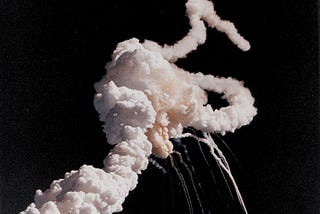 Color photograph of Challenger breaking apart in the air with visible plumes of steam.