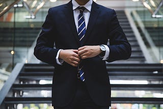 Torso of a person wearing a dark blue suit jacket, white collared shirt, and striped tie
