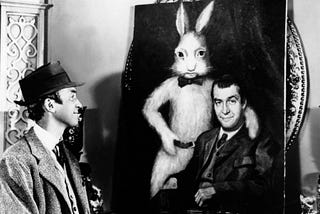 Frame from the film Harvey: Elwood P. Dowd smiling at a portrait of himself with his best friend Harvey, a 6-foot tall white rabbit