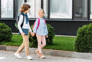 Boy and girl with backpacks walking on sidewalk