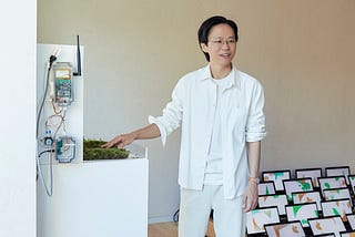 Taeyoon wearing white, in a room with many laptops that is displaying virtual garden