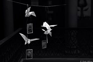 Black and white image of origami figures hanging on a wire with photographs of flowers attached to them.