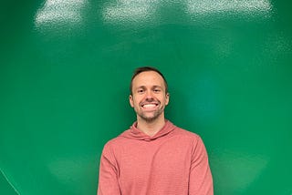 The author in a magenta-colored shirt in front of a green background.
