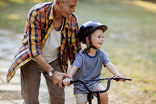 A grandfather teaching his grandson to ride a bike.