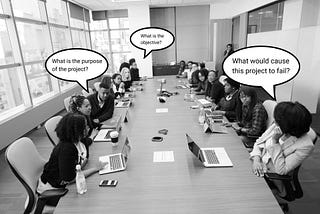 A team meeting on a large rectangular desk with roughly 20 colleagues on either side asking questions on the objective.