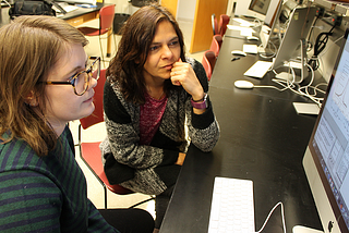 Jenna Harvey and her advisor, Anca Constantin, seated side by side and looking at a computer screen with a line graph.