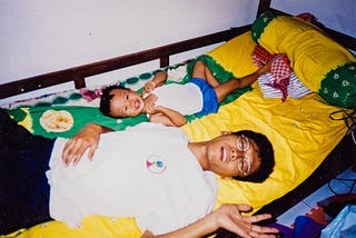 An analogue photograph of me and my dad. We were lying on a bed (covered with a yellow bed sheet), smiling to the camera.