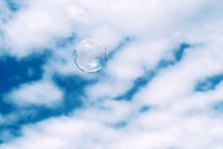 One soap bubble in front of a cloudy blue sky.