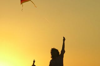 Silhouette of woman and child flying a rainbow kite against golden sky