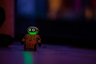 A small yellow robot toy with little wheels and bright eyes in the dusk on a table.