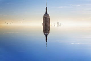 The Empire State building almost completely submerged in peaceful blue water that shows its reflection.