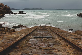 Image of an old railroad track that runs  into a body of water and disappears.