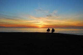 A couple sitting in camping chairs watching the sun set over the sea