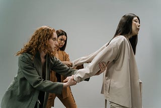 Two women hold a third woman back by her arms.