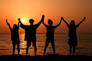 Friends holding hands near the ocean at sunset