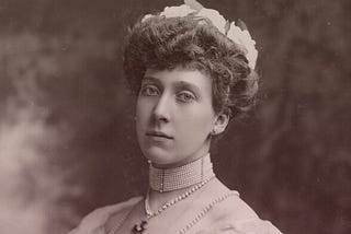 Marie Louise in a white day dress. Her thick dark-blonde hair is in a chignon, and she’s wearing a dog collar pearl choker.