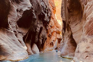 two people walking through water in between a canyon