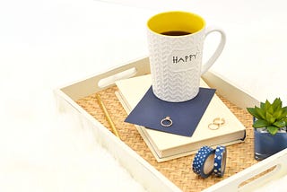 A book with washi tape, wedding rings and a “happy” mug in a tray.