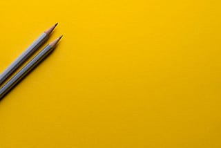 Two grey pencils on a yellow surface