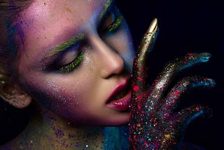 Woman wearing colorful makeup in hi-tech fashion. Her hand is painted gold with splashes of color.