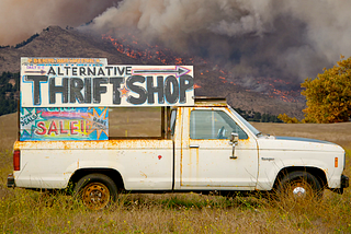 a truck with a sign to a thrift store sits in a field in front of a wild fire