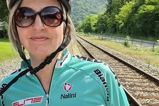 Lisa in front of a railway track in cycling gear. Green Bianchi shirt and silver helmet.