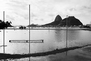 Uma foto em preto e branco que mostra o Pão de Açúcar e a baía de Guanabara com muitos barcos no fundo,