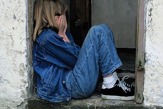 child sitting in a doorway, hands covering face