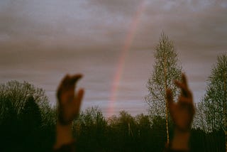 Hands raised up with rainbow in background