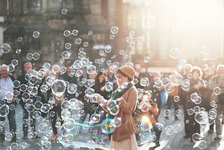 A woman in a tan coat, surrounded by bubbles. What’s her story? That’s sonder, friend.